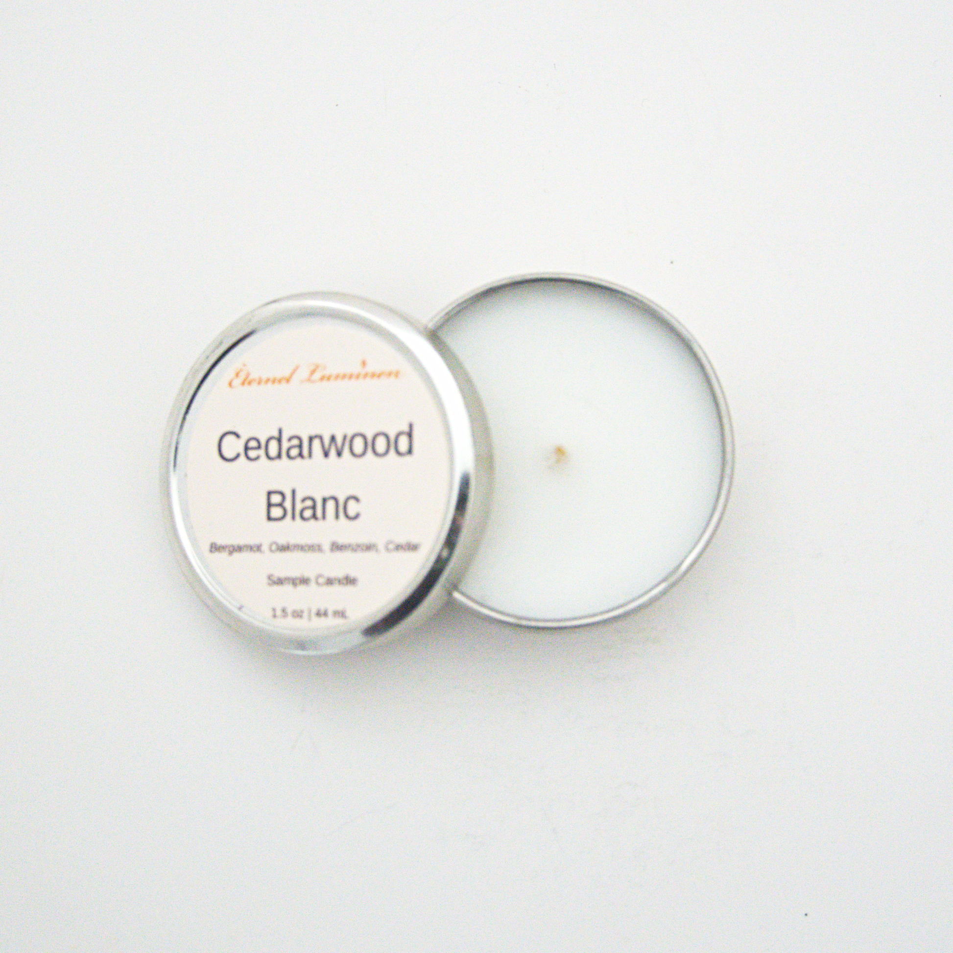 A 1.5oz Cedarwood Blanc sample candle in a tin jar with the lid off sitting against a white background made by Eternel Luminen.