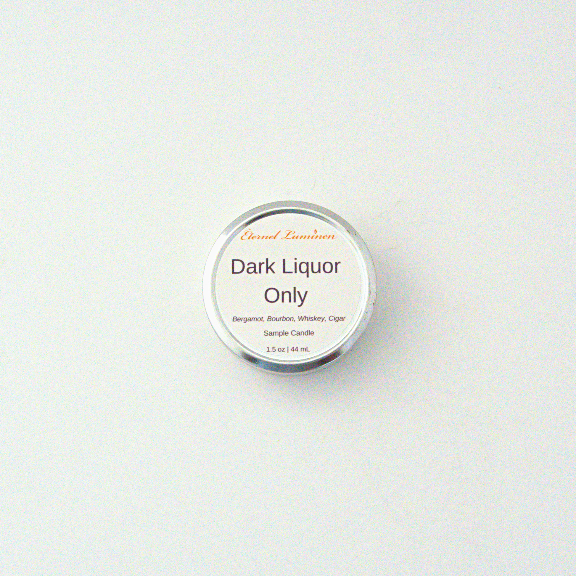 A 1.5oz Dark Liquor Only  sample candle in a tin jar sitting against a white background made by Eternel Luminen