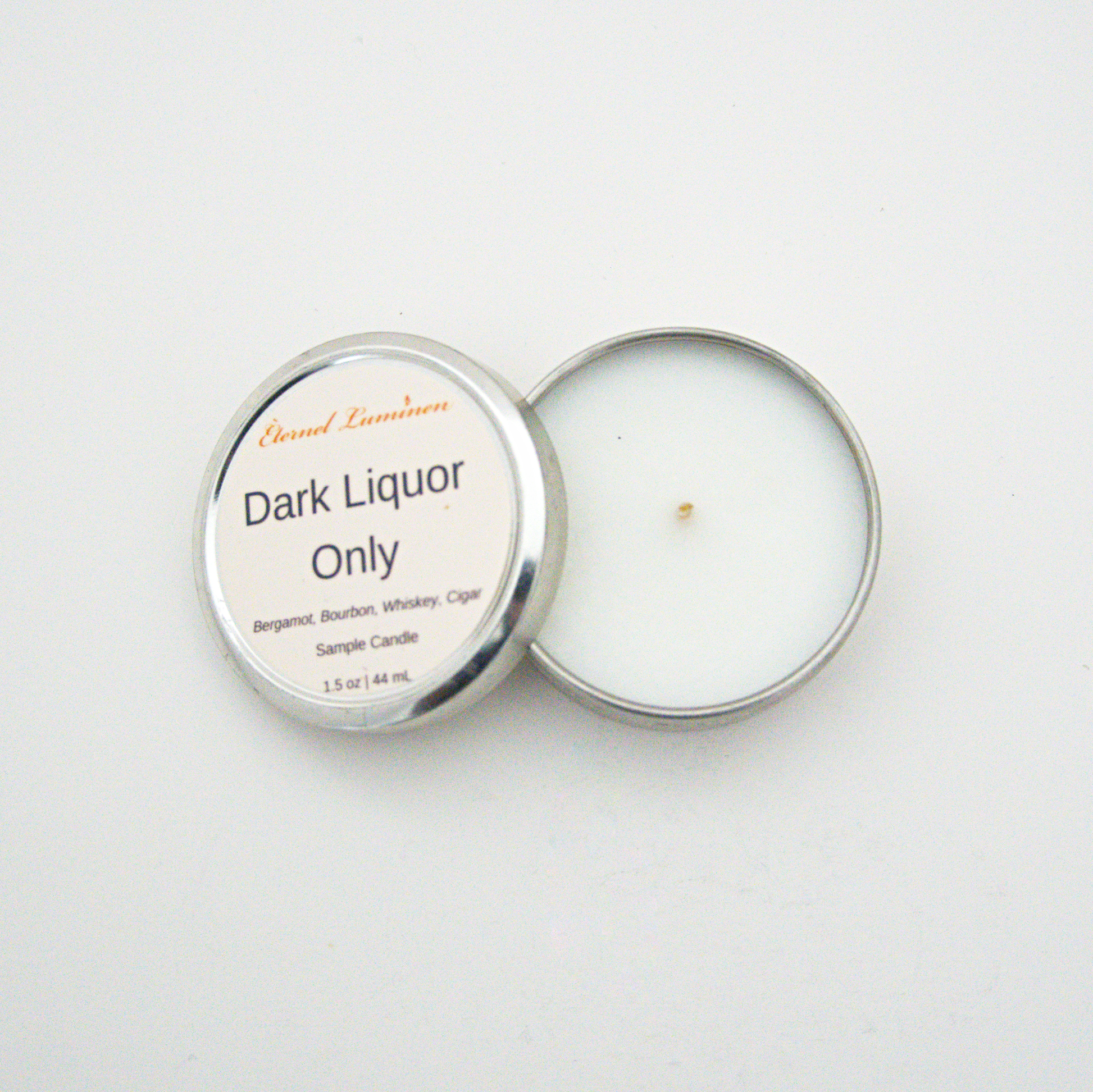 A 1.5oz Dark Liquor Only sample candle in a tin jar with the lid off sitting against a white background made by Eternel Luminen.