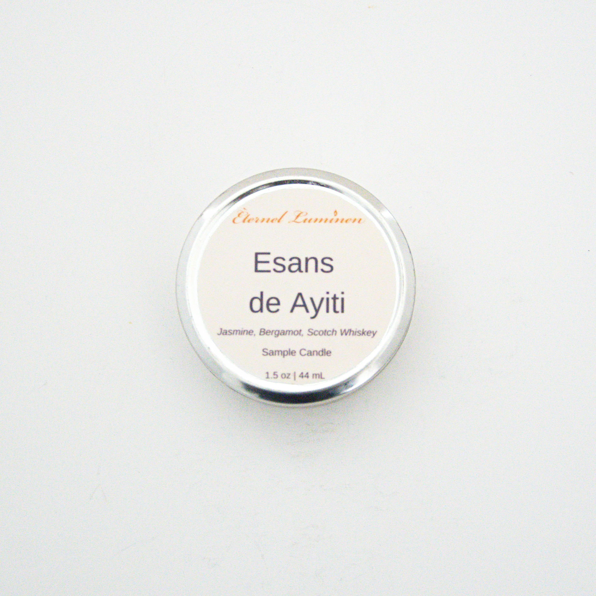 A 1.5oz Esans de Ayiti sample candle in a tin jar sitting against a white background made by Eternel Luminen