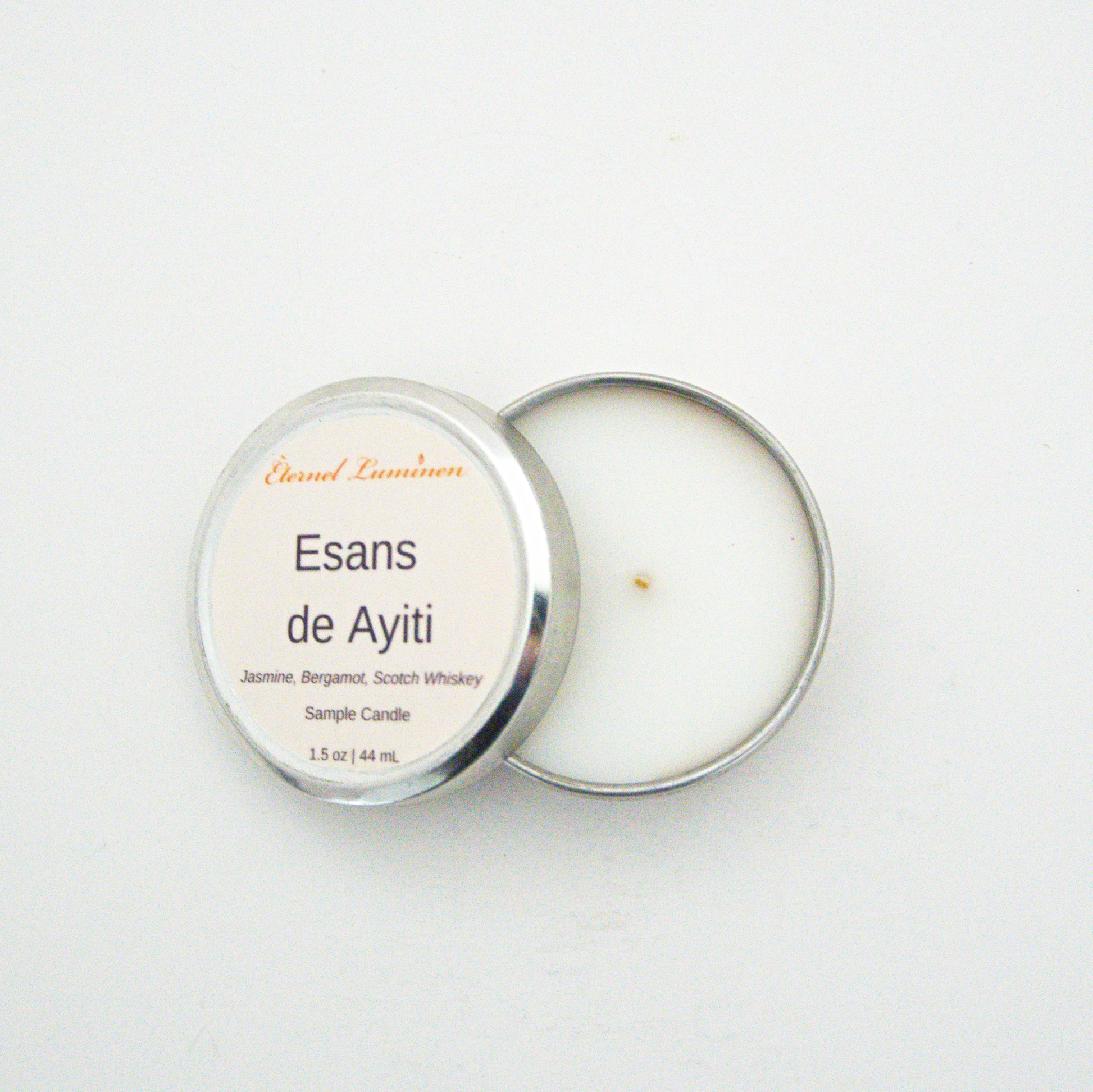 A 1.5oz Esans de Ayiti sample candle in a tin jar with the lid off sitting against a white background made by Eternel Luminen.