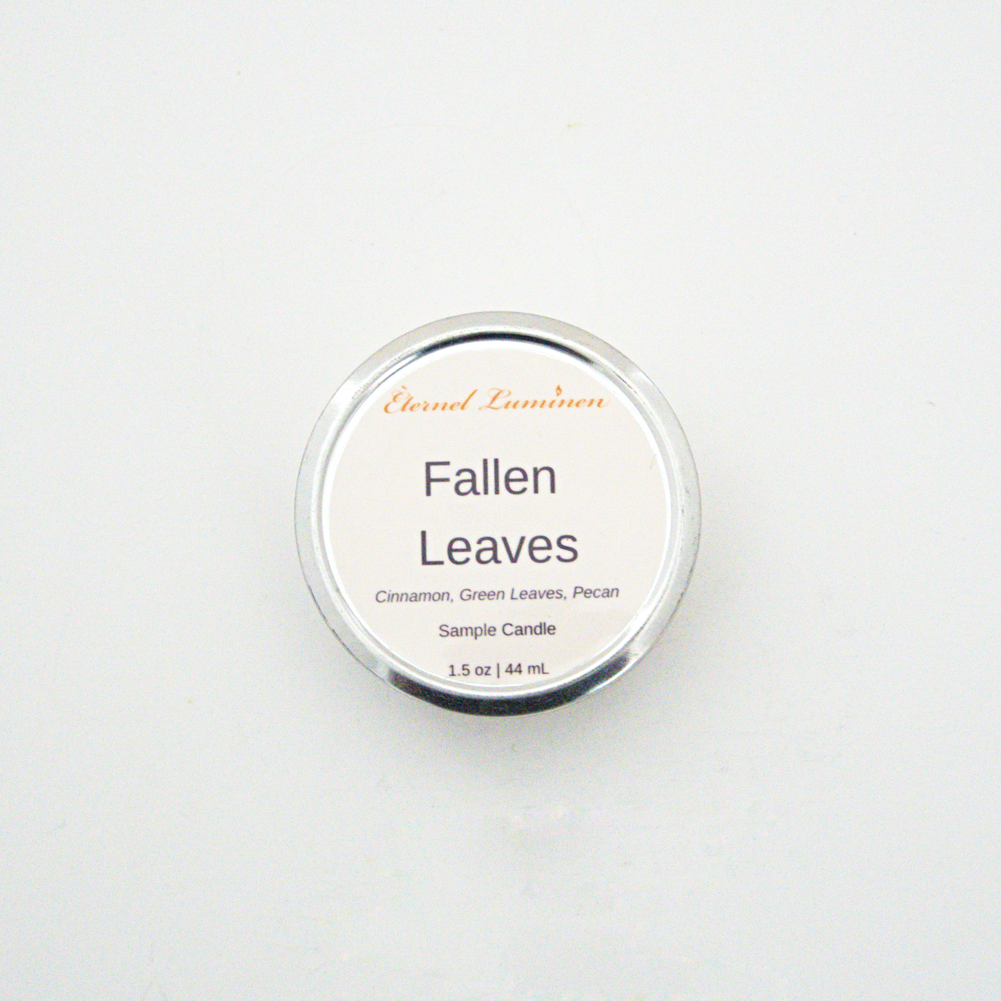 A 1.5oz Fallen Leaves sample candle in a tin jar sitting against a white background made by Eternel Luminen