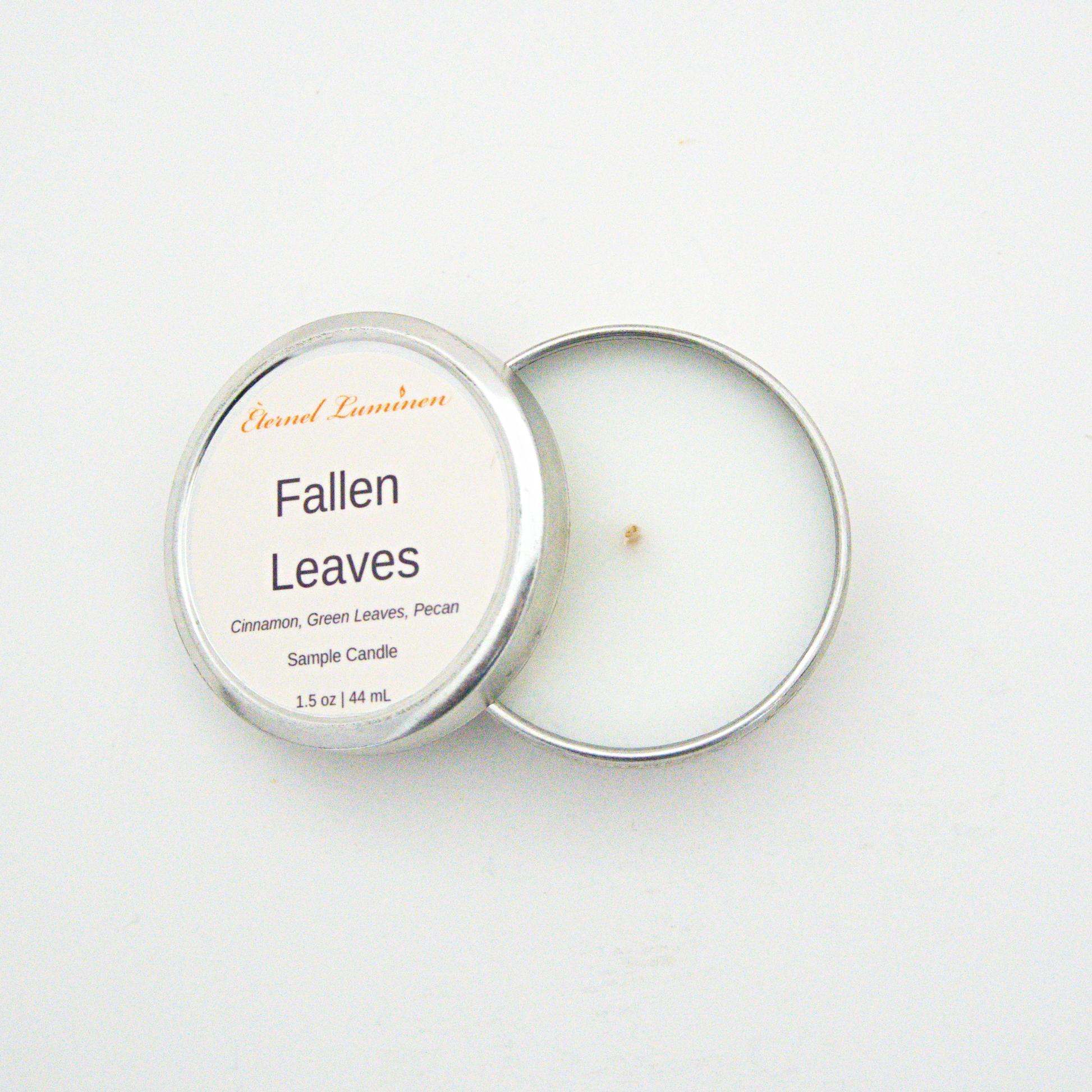 A 1.5oz Fallen Leaves sample candle in a tin jar with the lid off sitting against a white background made by Eternel Luminen.