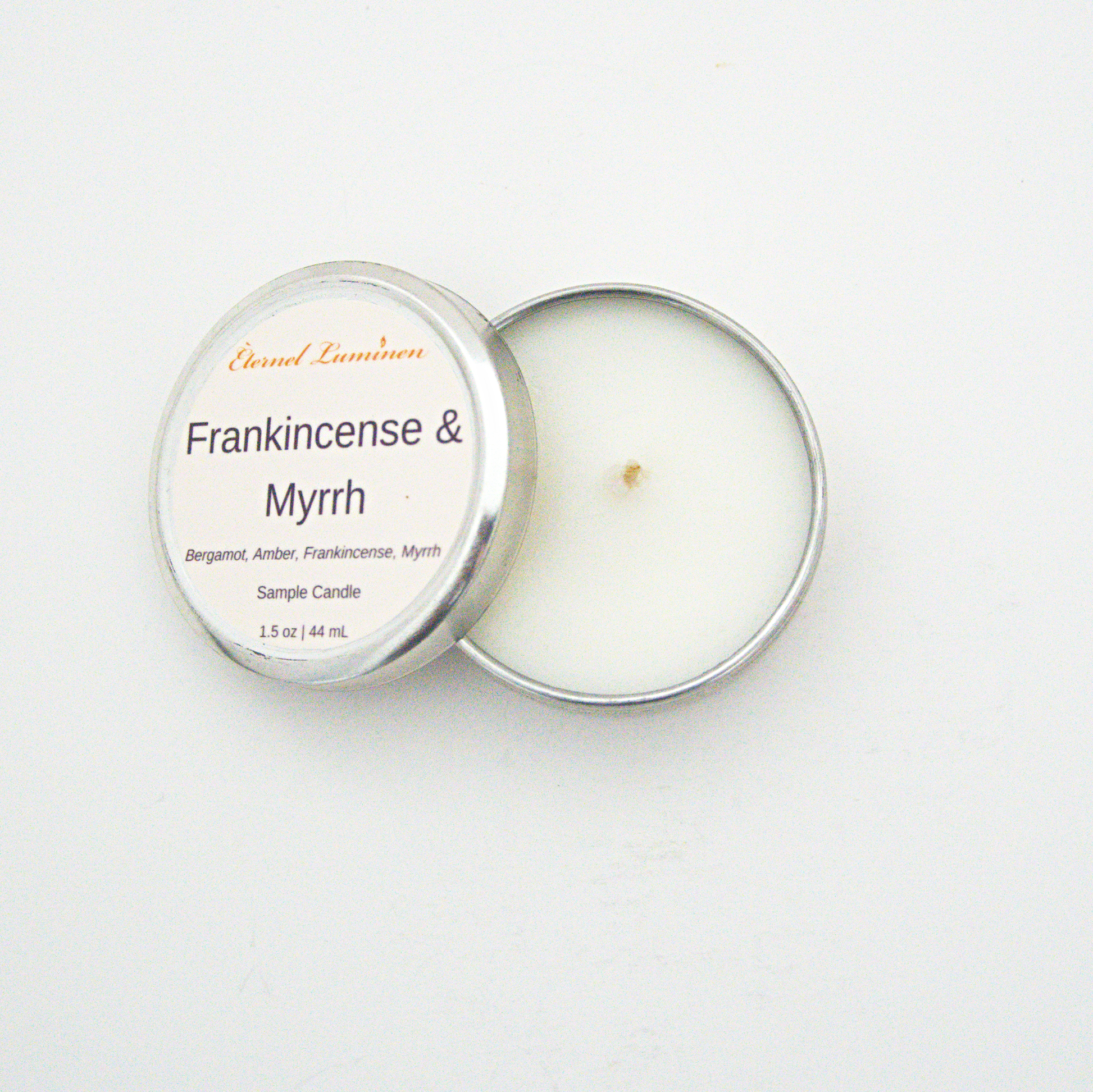 A 1.5oz Frankincense & Myrrh sample candle in a tin jar with the lid off sitting against a white background made by Eternel Luminen.
