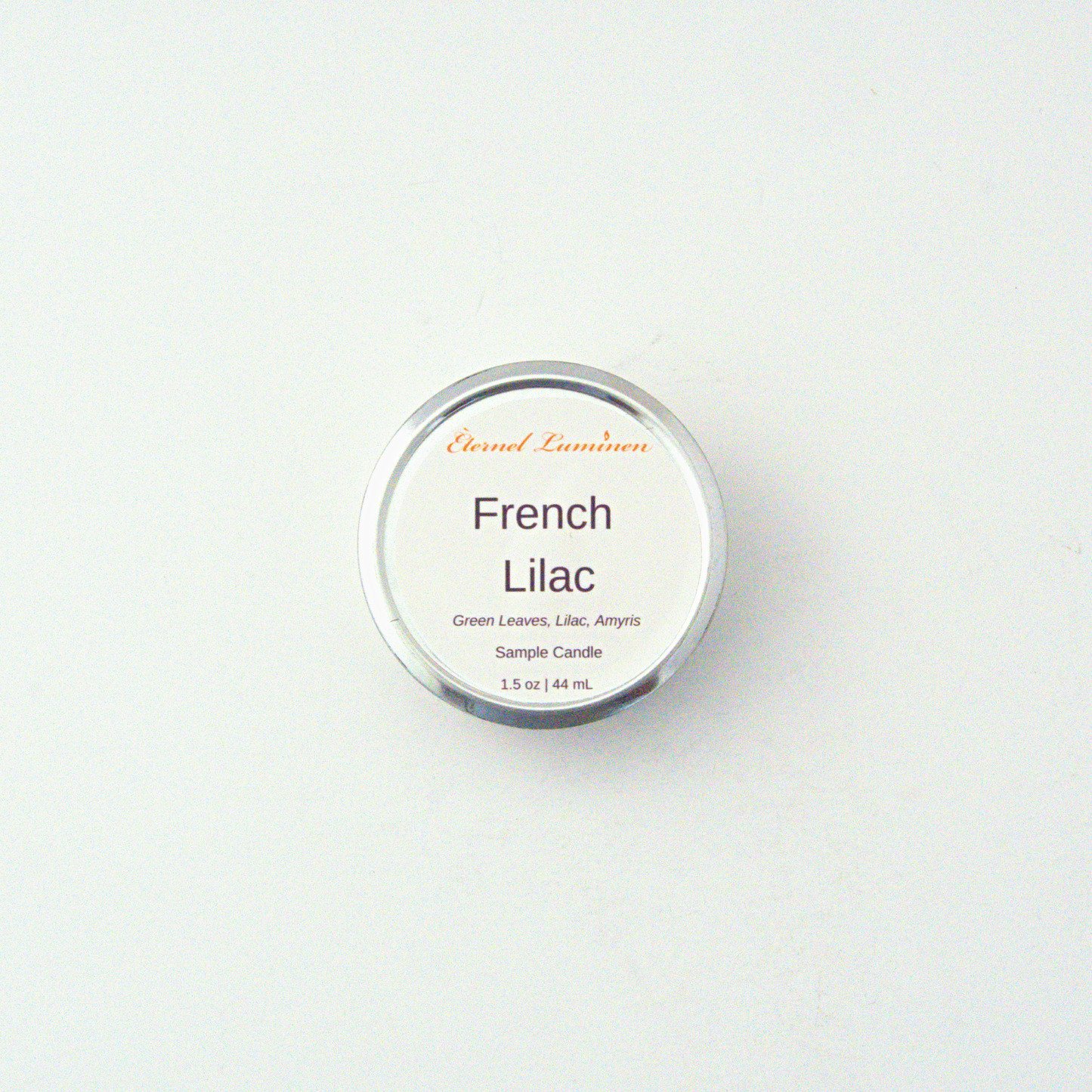A 1.5oz French Lilac sample candle in a tin jar sitting against a white background made by Eternel Luminen