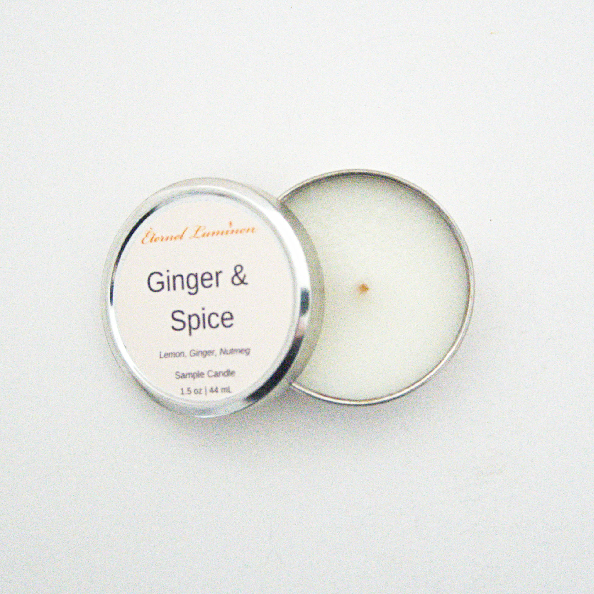A 1.5oz Ginger & Spice sample candle in a tin jar with the lid off sitting against a white background made by Eternel Luminen.