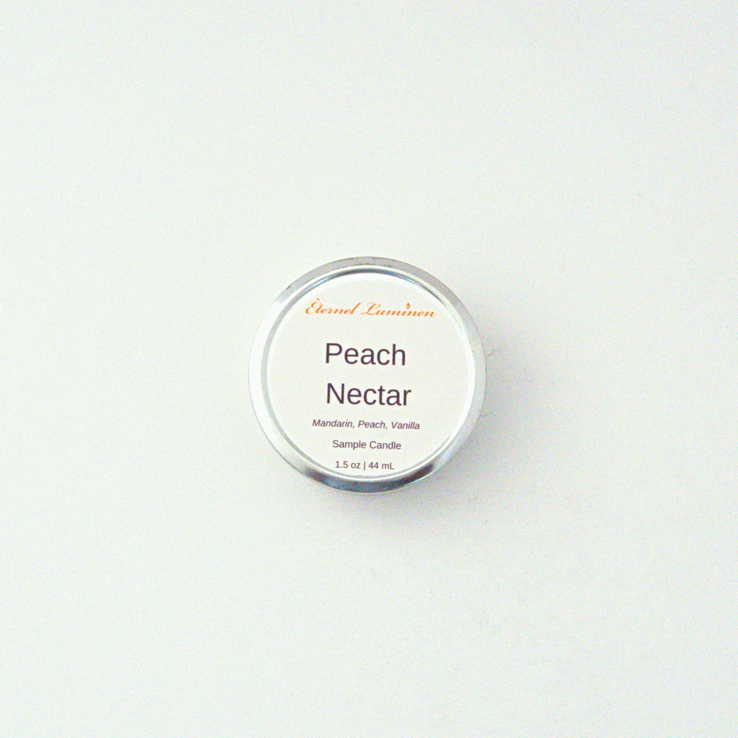 A 1.5oz Peach Nectar sample candle in a tin jar sitting against a white background made by Eternel Luminen