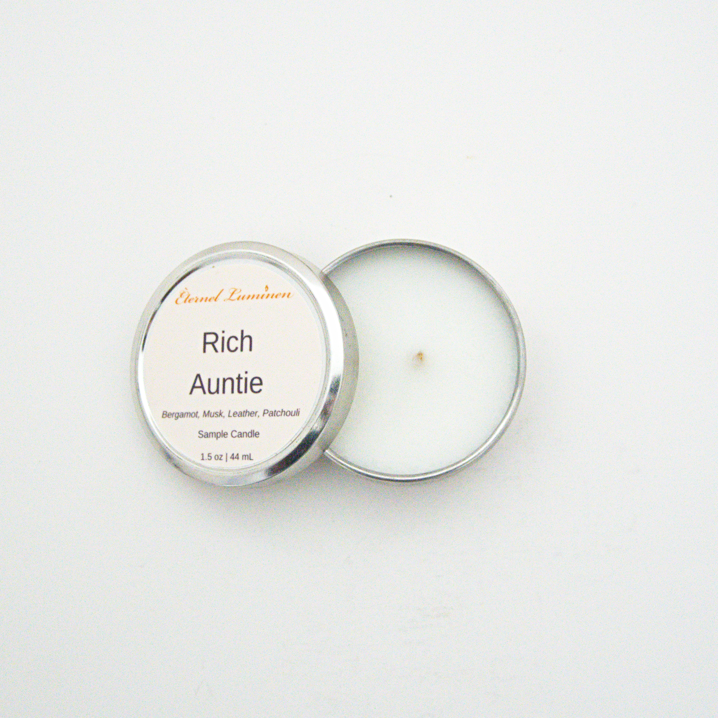 A 1.5oz Rich Auntie sample candle in a tin jar with the lid off sitting against a white background made by Eternel Luminen.