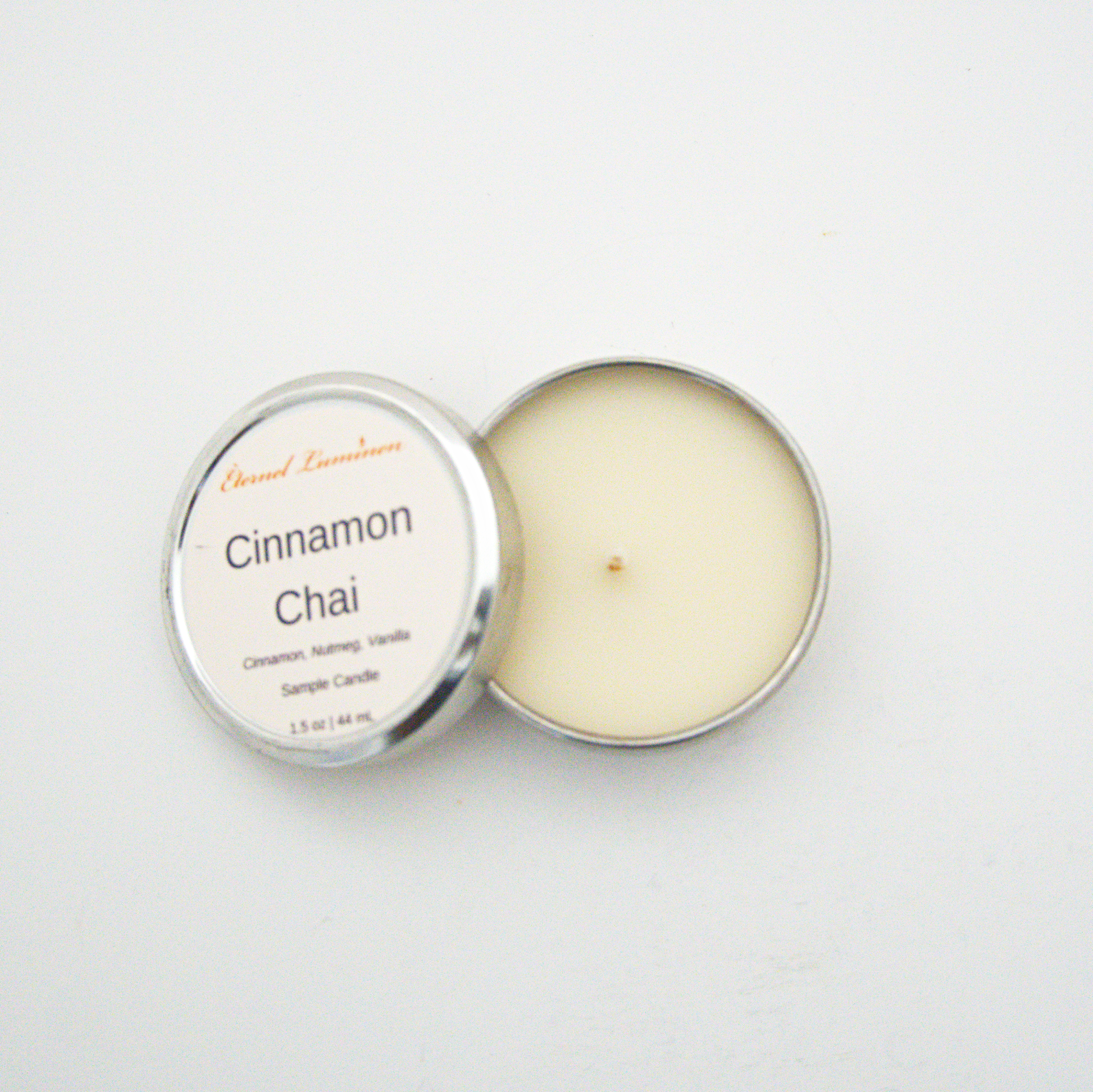 A 1.5oz Cinnamon Chai sample candle in a tin jar with the lid off sitting against a white background made by Eternel Luminen.