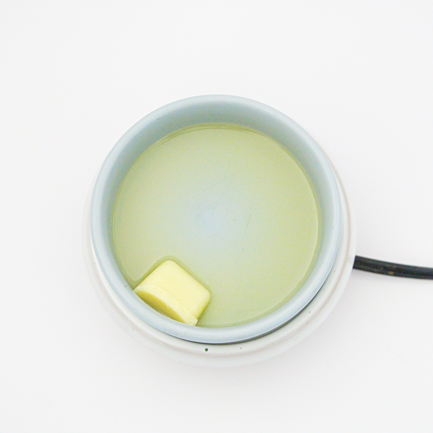 wax melt melting in a small ceramic wax warmer dish on a white background