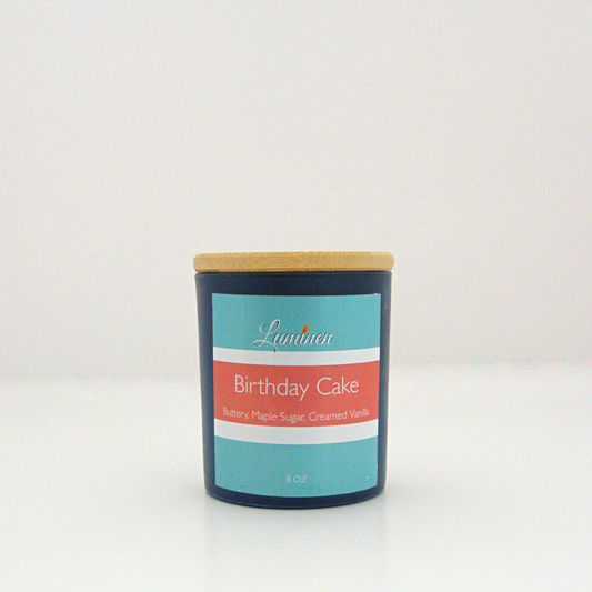 A 8 oz frosted Birthday Cake candle with a wooden lid sitting against a white background made by Eternel Luminen.