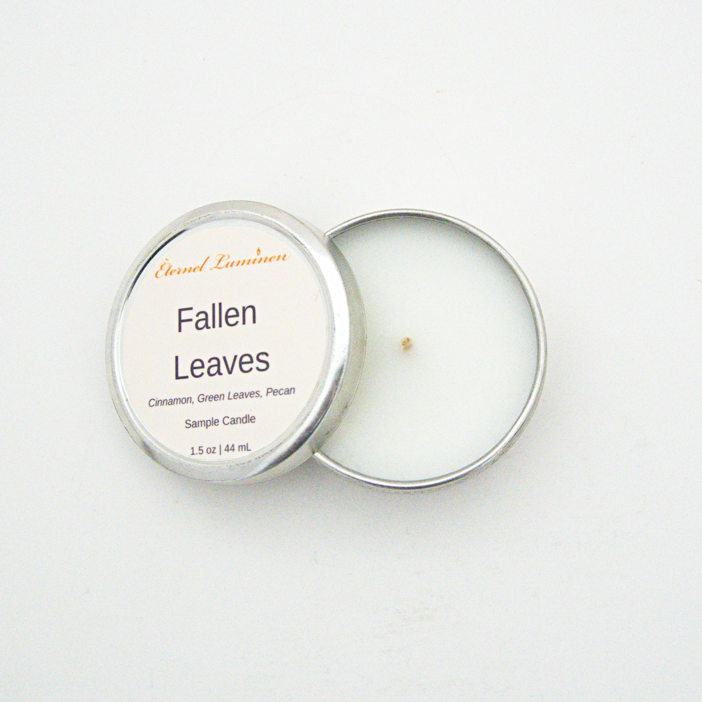 A 1.5oz Fallen Leaves sample candle in a tin jar with the lid off sitting against a white background made by Eternel Luminen.