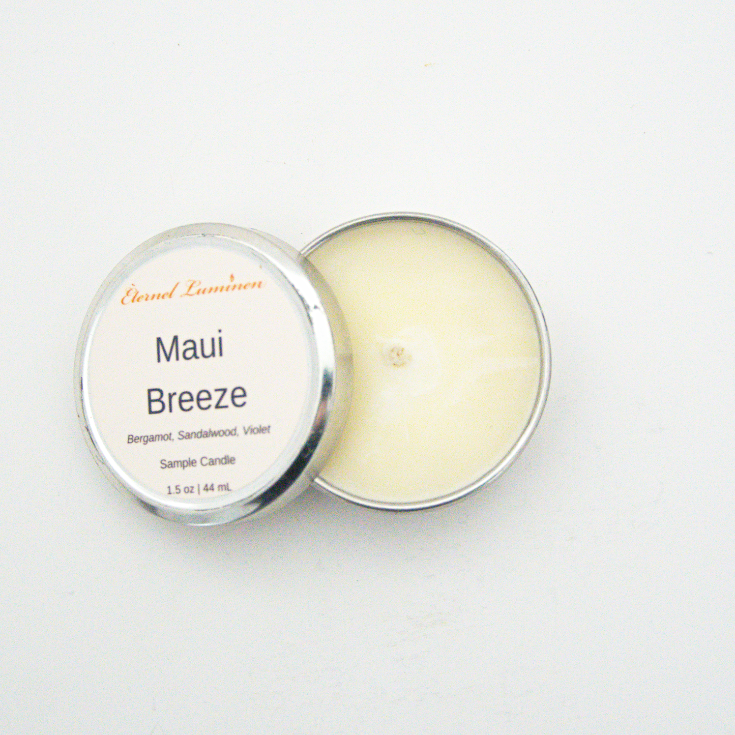 A 1.5oz Maui Breeze sample candle in a tin jar with the lid off sitting against a white background made by Eternel Luminen.