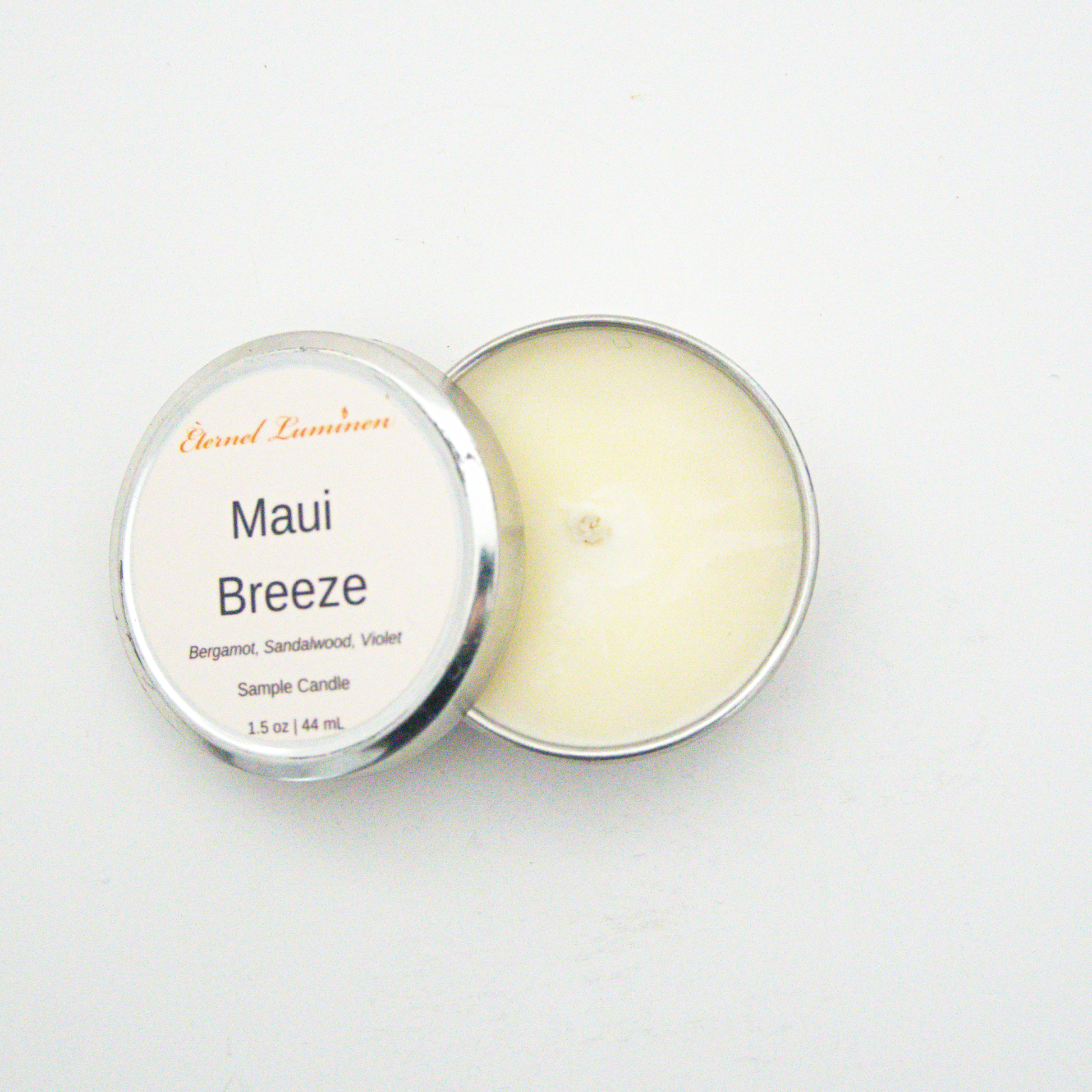 A 1.5oz Maui Breeze sample candle in a tin jar with the lid off sitting against a white background made by Eternel Luminen.