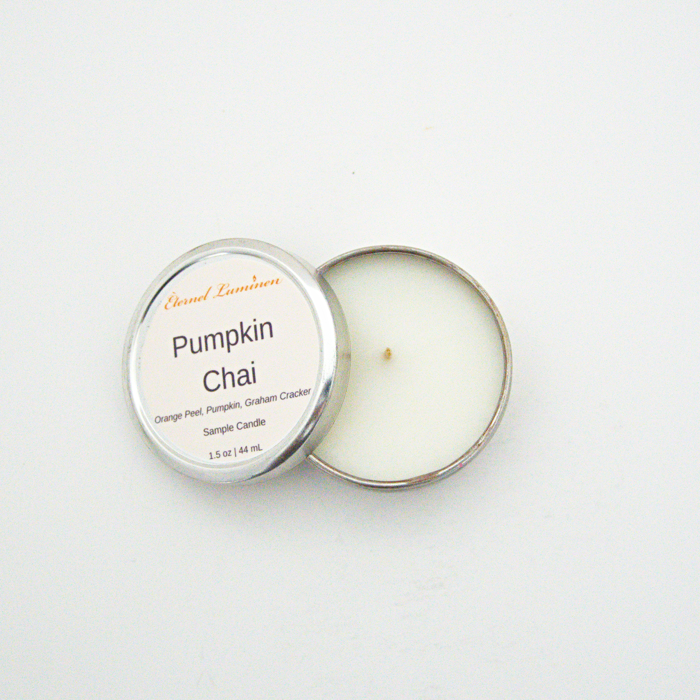 A 1.5oz Pumpkin Chai sample candle in a tin jar with the lid off sitting against a white background made by Eternel Luminen.