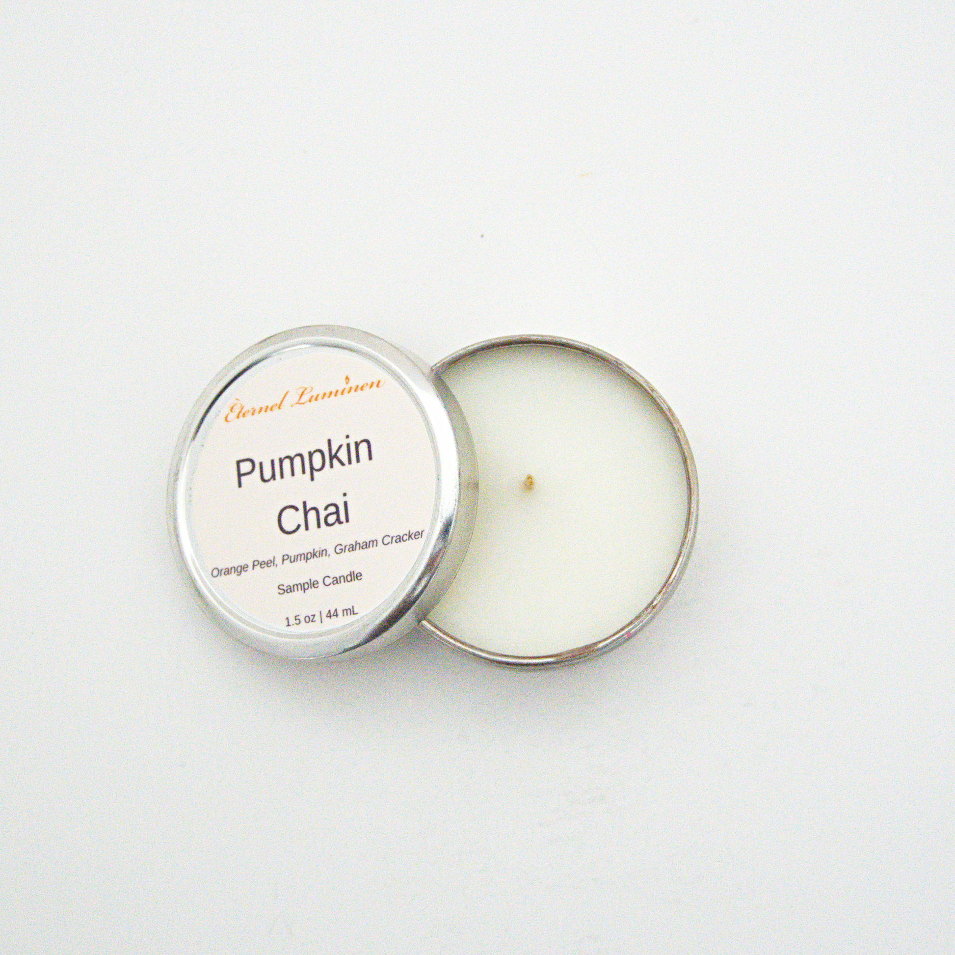 A 1.5oz Pumpkin Chai sample candle in a tin jar with the lid off sitting against a white background made by Eternel Luminen.