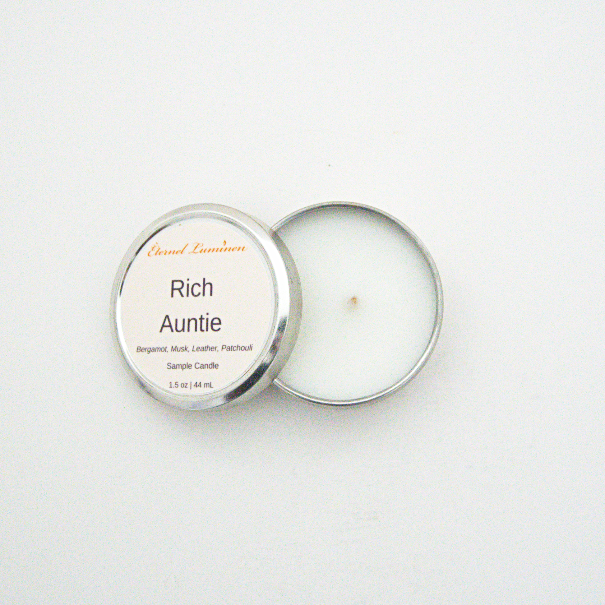 A 1.5oz Rich Auntie sample candle in a tin jar with the lid off sitting against a white background made by Eternel Luminen.