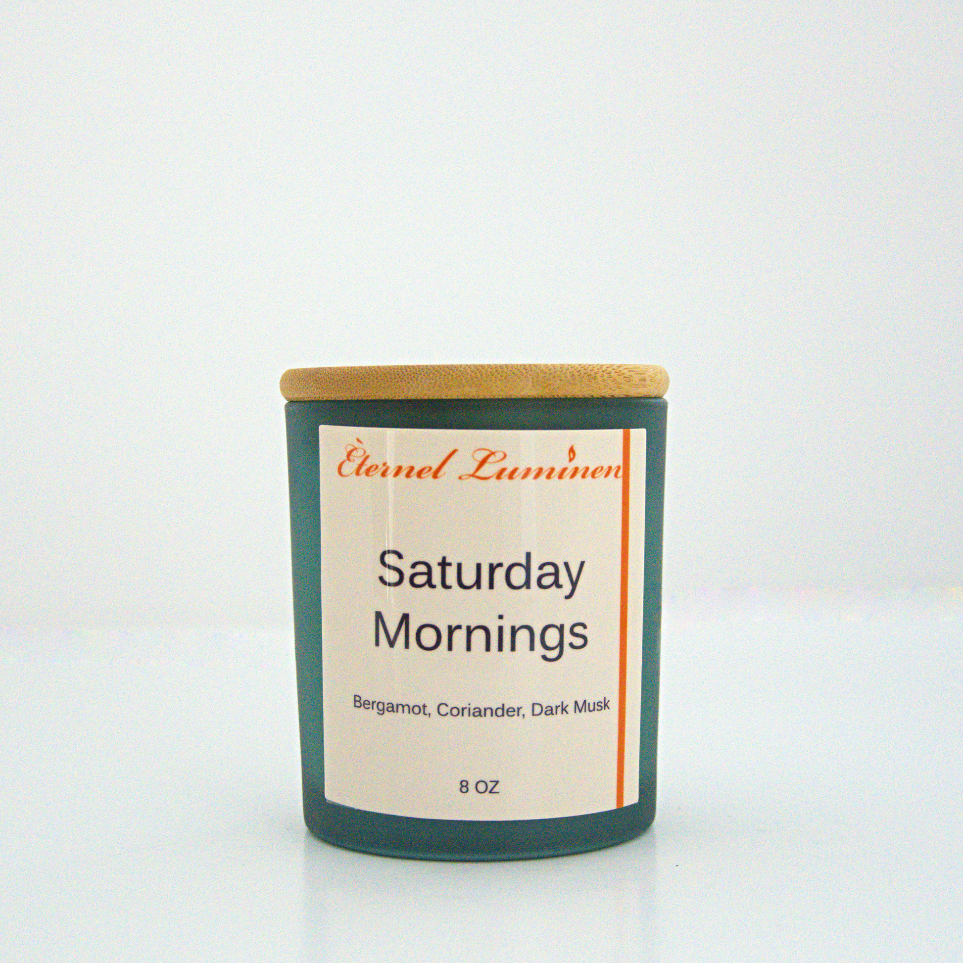 A 8 oz frosted Saturday Mornings candle with a wooden lid sitting against a white background made by Eternel Luminen.