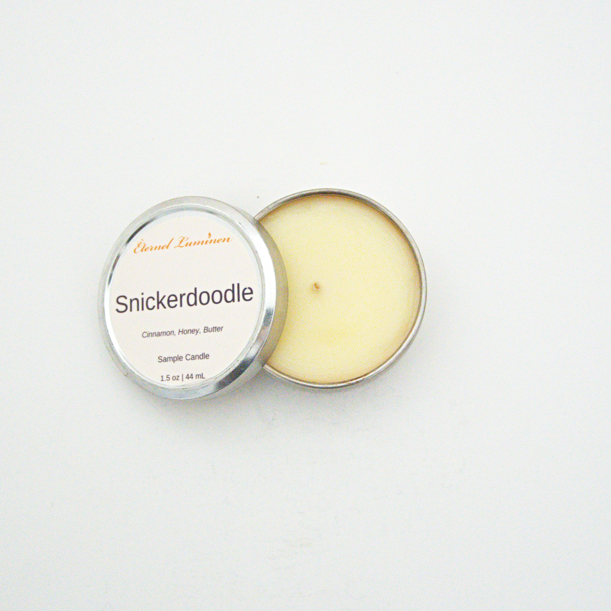 A 1.5oz Snickerdoodle sample candle in a tin jar with the lid off sitting against a white background made by Eternel Luminen.