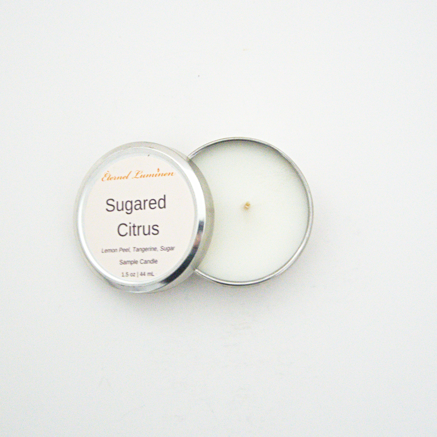 A 1.5oz Sugared Citrus sample candle in a tin jar with the lid off sitting against a white background made by Eternel Luminen.
