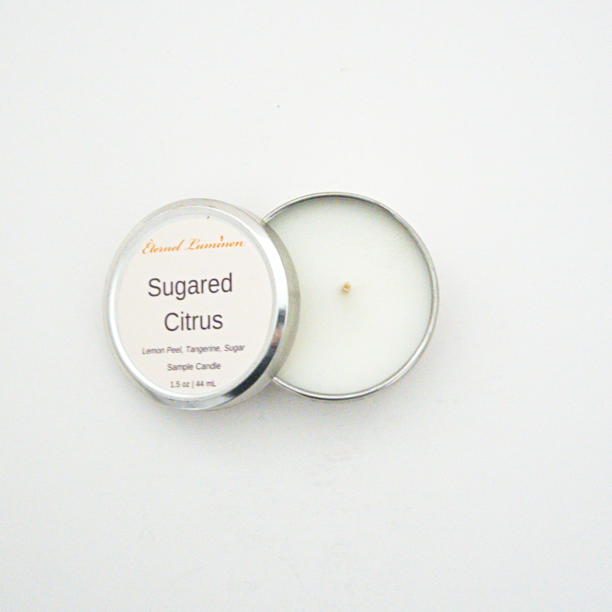A 1.5oz Sugared Citrus sample candle in a tin jar with the lid off sitting against a white background made by Eternel Luminen.
