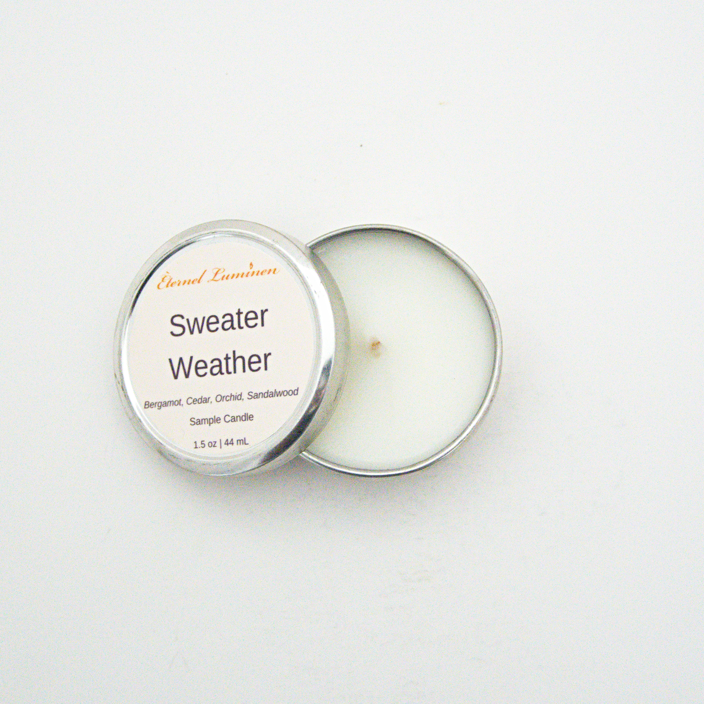 A 1.5oz Sweater Weather sample candle in a tin jar with the lid off sitting against a white background made by Eternel Luminen.