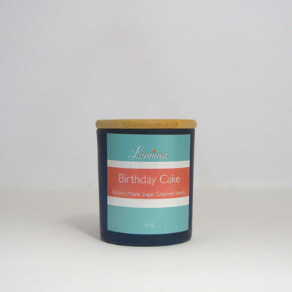 A 8 oz frosted Birthday Cake candle with a wooden lid sitting against a white background made by Eternel Luminen.