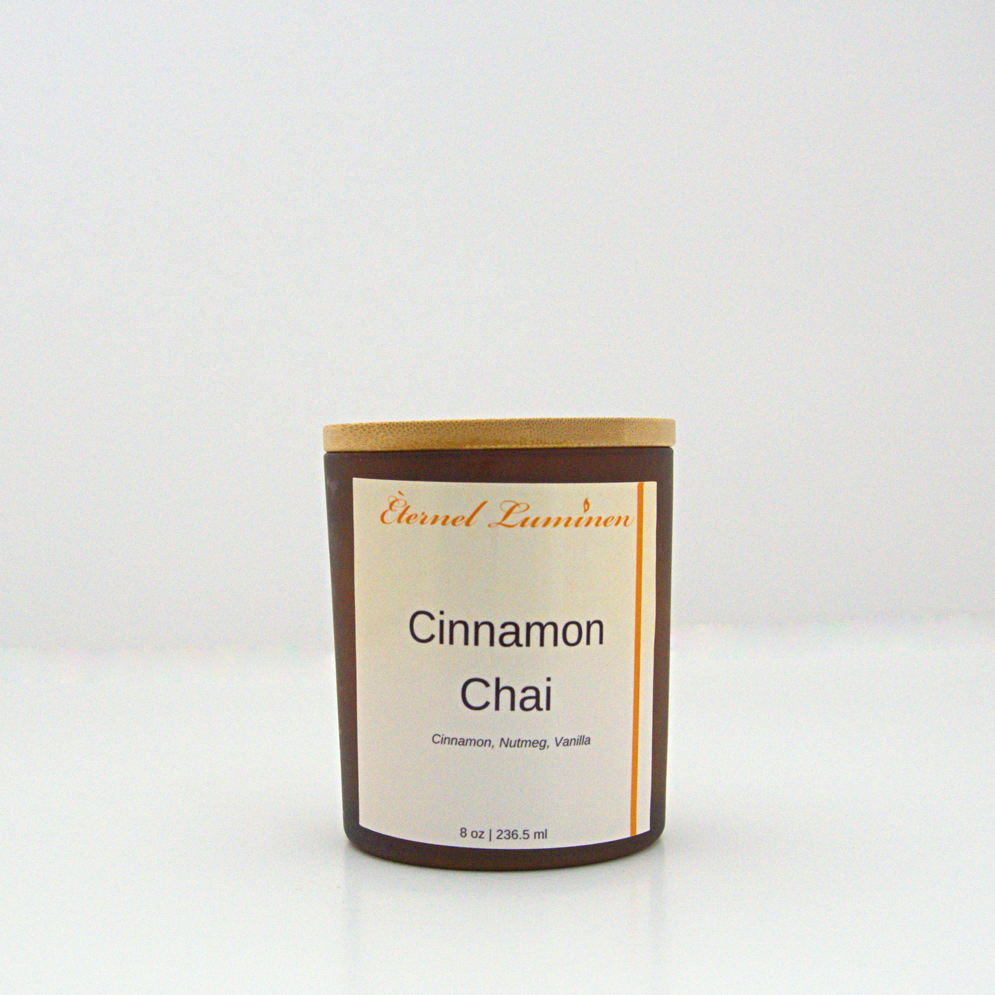 A 8 oz frosted Cinnamon Chai candle with a wooden lid sitting against a white background made by Eternel Luminen.