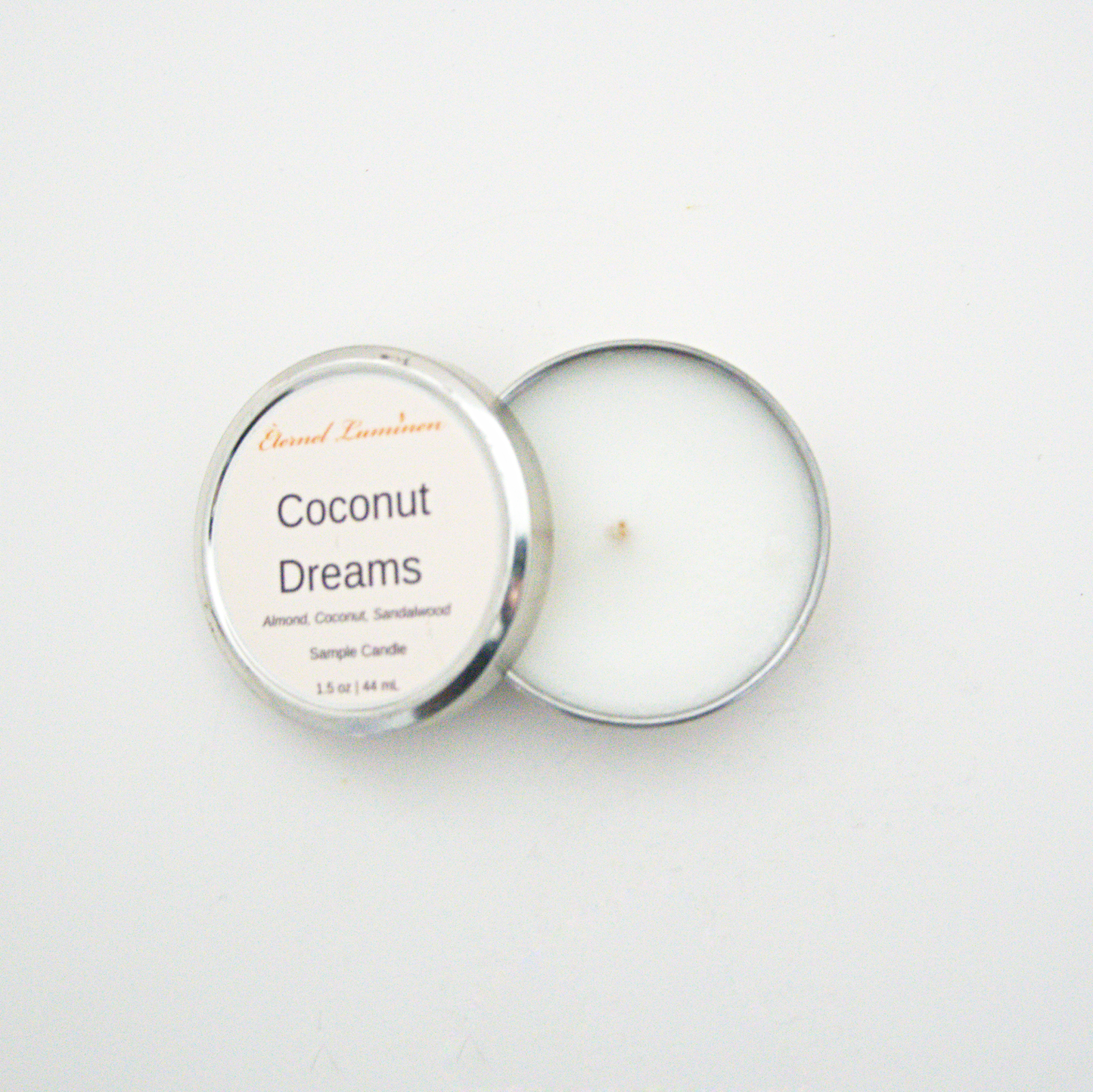 A 1.5oz Coconut Dreams sample candle in a tin jar with the lid off sitting against a white background made by Eternel Luminen.